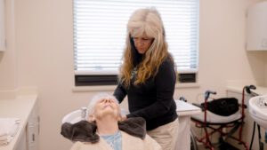 A woman getting her hair done by a stylist at the salon available at BirchPointe, a skilled nursing facility
